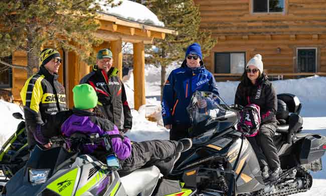 Adults take a break while snowmobiling near log buildings