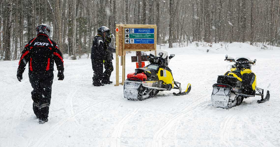 Snowmobiles in New Hampshire ride past signs that are part of grant program.